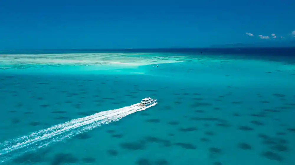 A boat cutting a wake across a shallow reef flat seen from above