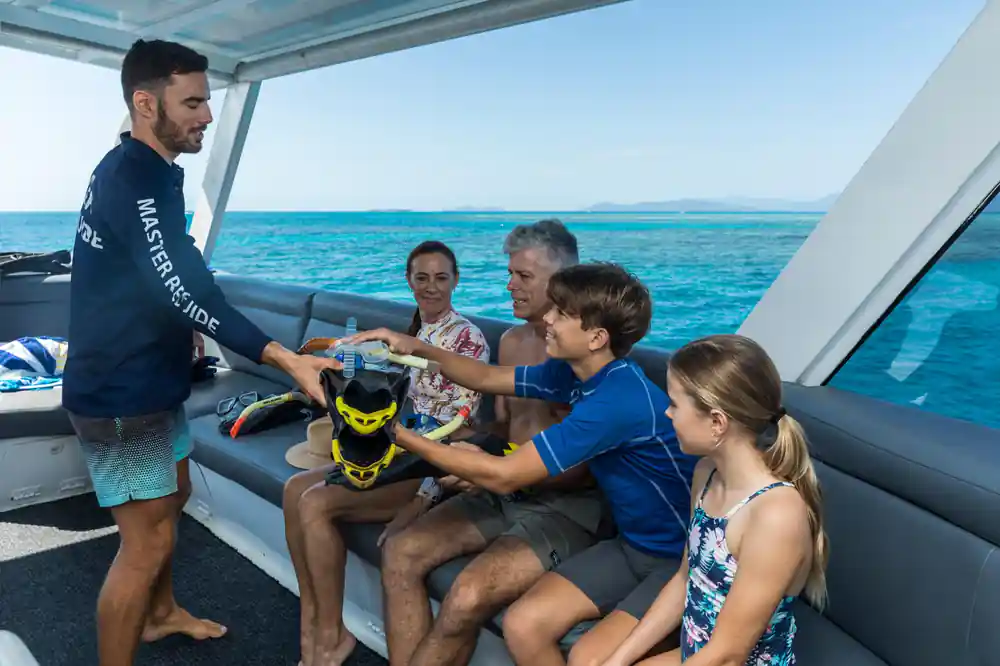 A family being handed snorkelling gear on the boat's rear seating