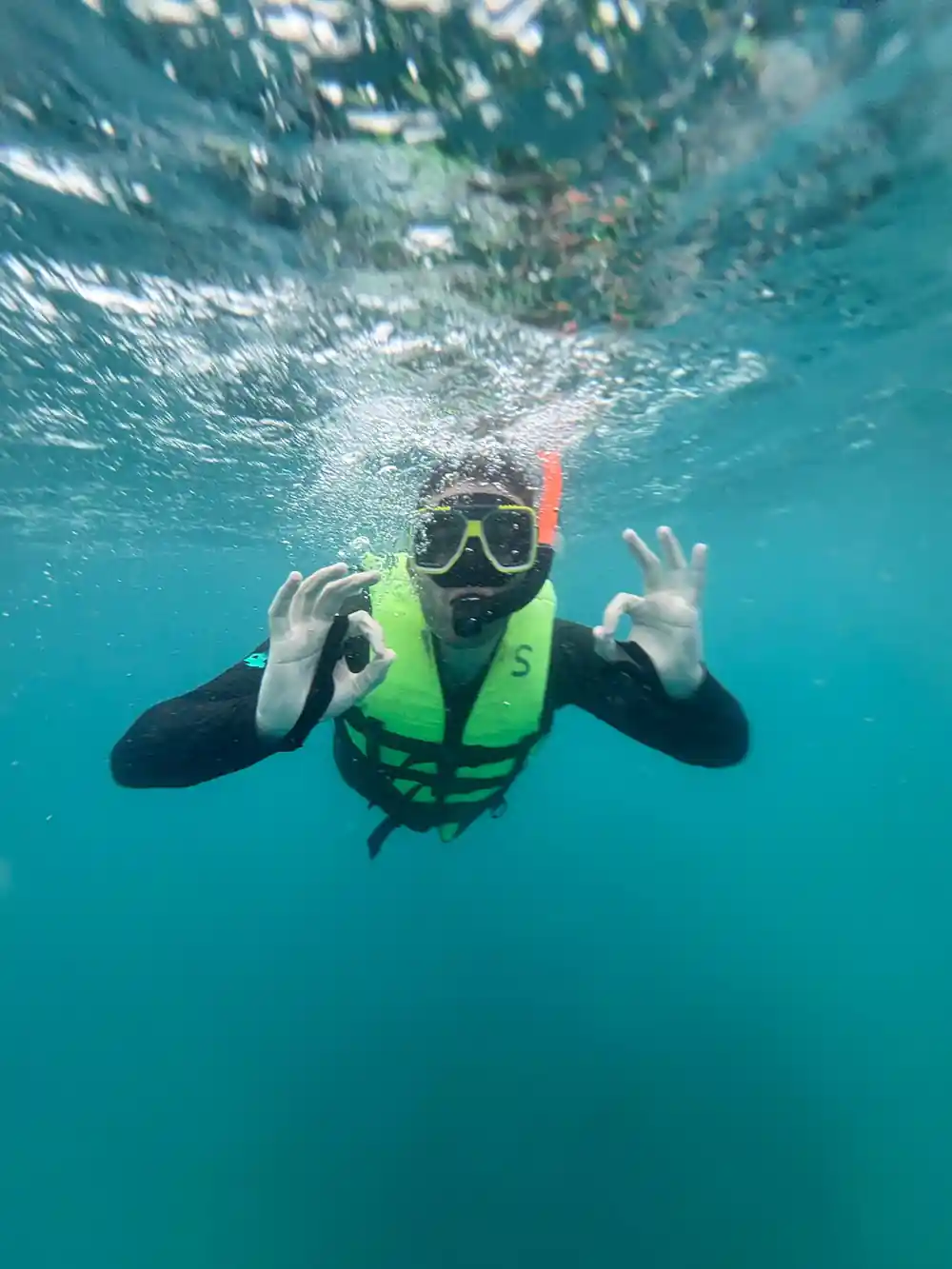 A snorkeller in a flotation vest giving both okay signs underwater