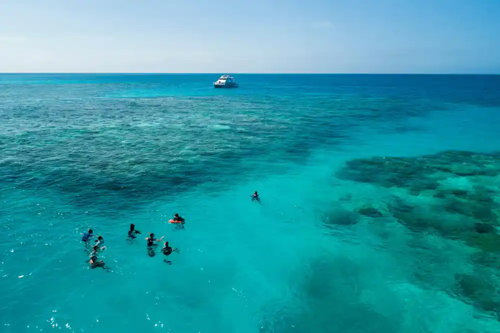 Swimmers in turquoise shallows with the boat anchored behind